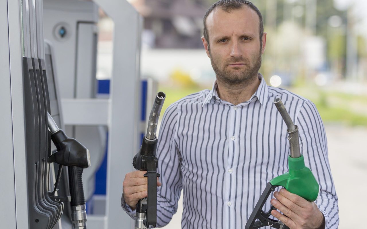 Homme mécontent à la station essence qui tient deux pompes différentes