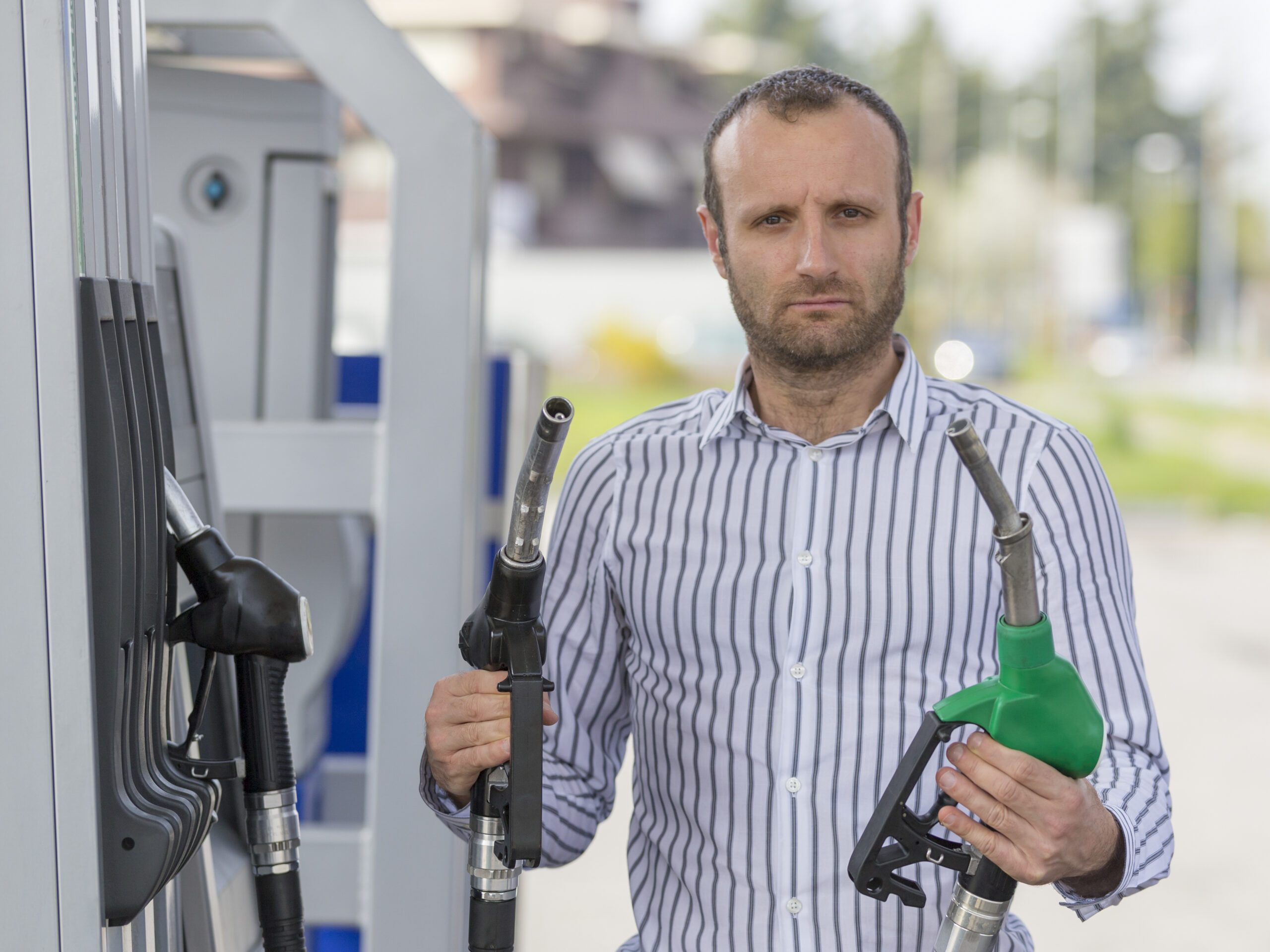 Homme mécontent à la station essence qui tient deux pompes différentes